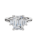 An 18K white gold engagement ring with a central emerald-cut stone, accented by two rectangular side stones (0.125TCW), displayed on a plain white background.