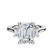 An 18K white gold engagement ring with a central emerald-cut stone, accented by two rectangular side stones (0.125TCW), displayed on a plain white background.