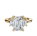 The 14K Yellow Gold 3-Stone Emerald Cut Side Stones 0.125TCW Engagement Ring features a center emerald-cut diamond with two smaller rectangular diamonds on each side, all set in a classic four-prong setting.