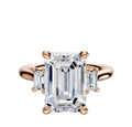 The 18K Rose Gold 3-Stone Emerald Cut Side Stones 0.25TCW Engagement Ring features a central emerald-cut gemstone and two smaller rectangular side stones in a four-prong rose gold setting.