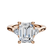 The 18K Rose Gold 3-Stone Engagement Ring features a large center stone with 0.125TCW trillion side stones, shown against a plain white background.