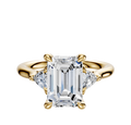 The 14K Yellow Gold 3-Stone Trillion Side Stones 0.125TCW Engagement Ring showcases a center diamond accented by two smaller trillion-cut side stones, all set on a polished gold band against a white background.
