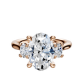 The 14K Rose Gold 3-Stone Oval Side Stones Engagement Ring features a large center oval diamond with two smaller round side stones (0.125TCW), set in elegant prongs against a white background.