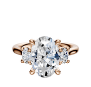 The 18K Rose Gold 3-Stone Oval Side Stones 0.125TCW Engagement Ring features an oval center diamond flanked by two round side diamonds in a prong setting, displayed on a plain white background.