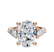 The 18K Rose Gold 3-Stone Pear Side Stones 0.25TCW Engagement Ring showcases a large oval center diamond with two pear-cut side diamonds, all set in elegant prongs against a simple background.
