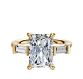 An 18K yellow gold engagement ring with a central radiant-cut diamond and two baguette side stones (0.125TCW), displayed on a plain white background.