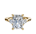 The 18K Yellow Gold 3-Stone Trillion Side Stones 0.125TCW Engagement Ring showcases a radiant center diamond flanked by two trillion-cut side stones in a four-prong setting, displayed against a plain white background.
