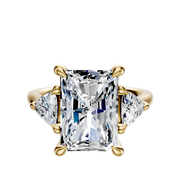 The 18K Yellow Gold 3-Stone Engagement Ring features a central radiant-cut diamond with two trillion side stones (0.25TCW), each set in gold prongs against a plain white background.