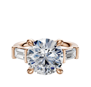 The 14K Rose Gold 3-Stone Baguette East/West Side Stones 0.25TCW Engagement Ring features a central round diamond flanked by two rectangular baguette diamonds in a four-prong setting, shown on a white background.