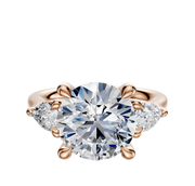 The 14K Rose Gold 3-Stone Pear Side Stones 0.25TCW Engagement Ring features a central round diamond accented by two pear-shaped side diamonds, all set in an elegant four-prong setting.