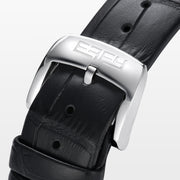 The 39MM Swiss Made Stainless Steel Signature Panther Watch with Diamonds features a jeweled panther design on the dial, gold and diamond accents, green gemstone eyes, and a black leather strap.