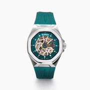 The 42MM Swiss Made Stainless Steel Automatic Skeleton Watch with Diamonds features a teal rubber strap, silver case, partially transparent dial with visible gears, teal bezel and markings, and EBFY branding at the top.