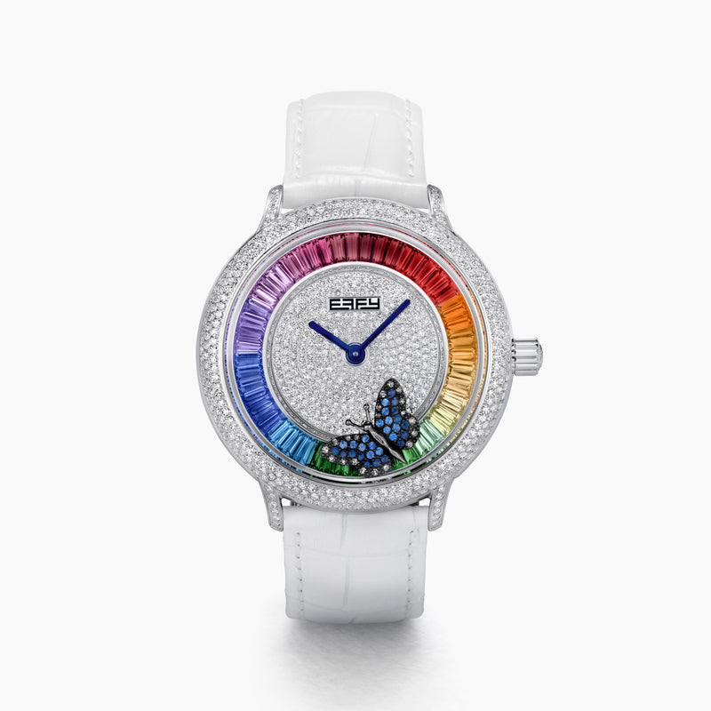 The 38MM Swiss Made Stainless Steel Rainbow Spinning Butterfly Watch features a pavé diamond face, rainbow gemstone bezel, white strap, and a butterfly adorned with blue and green gemstones at the bottom of the dial.