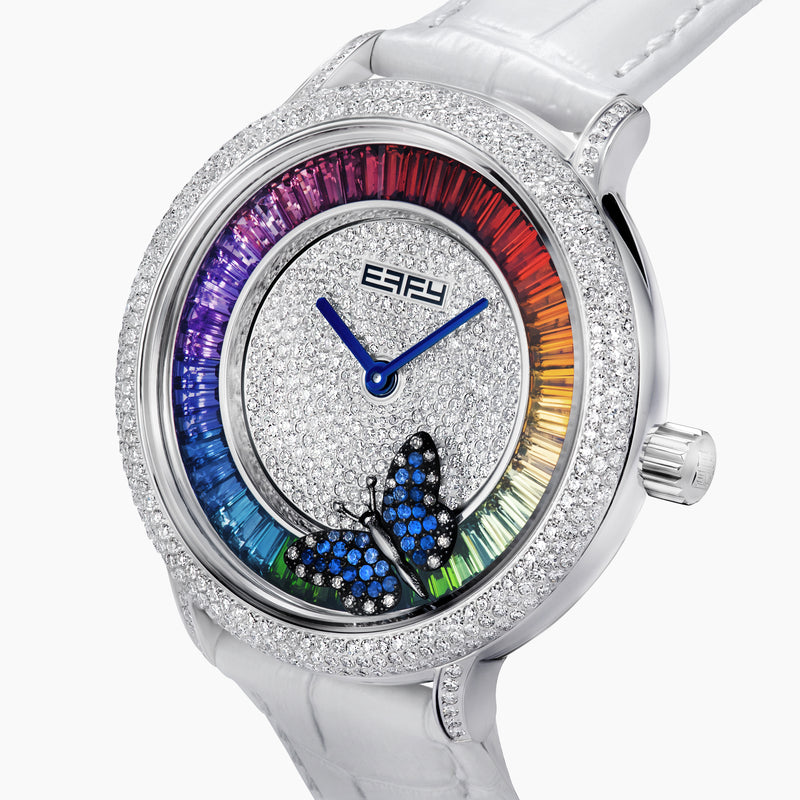 The 38MM Swiss Made Stainless Steel Rainbow Spinning Butterfly Watch features a pavé diamond face, rainbow gemstone bezel, white strap, and a butterfly adorned with blue and green gemstones at the bottom of the dial.