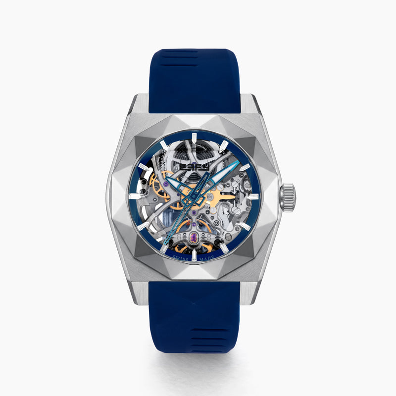 Introducing the 42MM Swiss Made Titanium and Silicone Automatic Skeleton Watch—a luxurious timepiece featuring a geometric silver titanium case and exposed inner mechanisms. Accented with a blue bezel and paired with a blue silicone strap, this design stands out against a white backdrop. Its exceptional clarity and elegance are enhanced by a diamond-cut sapphire crystal.