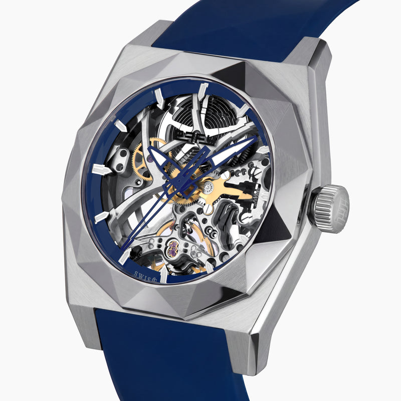 Introducing the 42MM Swiss Made Titanium and Silicone Automatic Skeleton Watch—a luxurious timepiece featuring a geometric silver titanium case and exposed inner mechanisms. Accented with a blue bezel and paired with a blue silicone strap, this design stands out against a white backdrop. Its exceptional clarity and elegance are enhanced by a diamond-cut sapphire crystal.