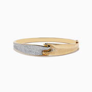 The DOro 14k Yellow Gold Pave Diamond Bangle showcases a unique design with one side encrusted in pave diamonds and the other in brushed gold, meeting at the center in a smooth, curved overlap.