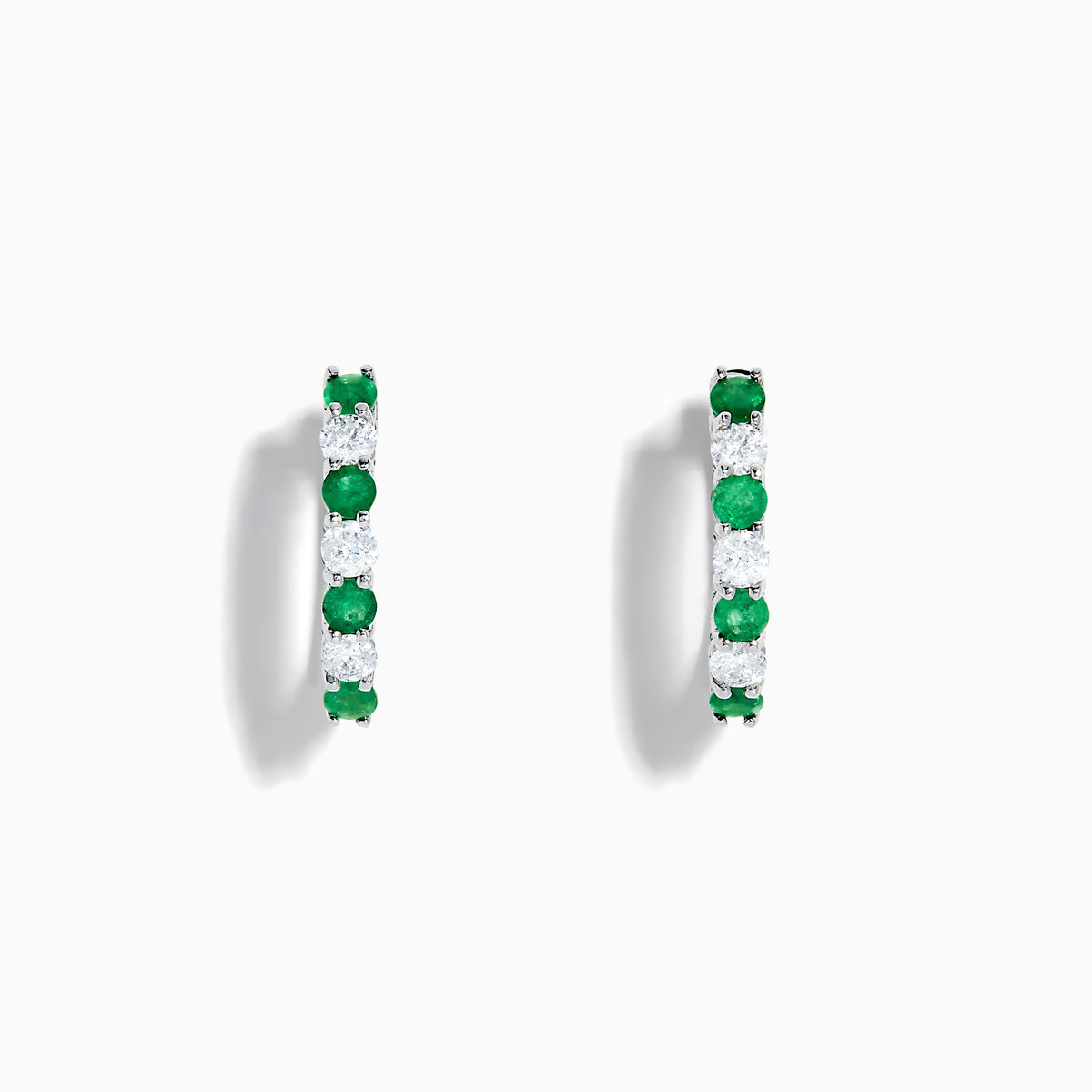 A pair of 14K white gold emerald & diamond hoop earrings, 1.10 TCW, featuring alternating green and clear gemstones set in a silver band, displayed on a white background with soft shadows.