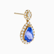 The Nahla 14K Yellow Gold Tanzanite and Diamond Drop Earrings feature teardrop-shaped blue tanzanite gems encircled by white diamonds, with extra diamonds set in the round studs, shown against a white background.