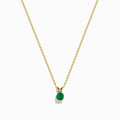 The 14K Yellow Gold Solitaire Round Emerald Pendant (0.48 TCW) features a delicate gold chain and a small round emerald, showcased against a white background.