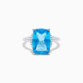 The Ocean Bleu 14K White Gold Blue Topaz and Diamond Ring showcases a large rectangular Blue Topaz gemstone, accented by sparkling diamonds on either side of the band.