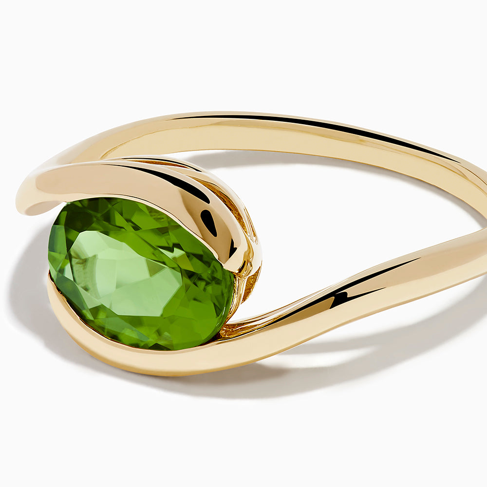 The 14K Yellow Gold Bypass Peridot Ring features a large round faceted green peridot centered on an elegant modern twisting band.