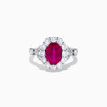 The 18K White Gold Ruby and Diamond Halo Ring features an oval red ruby at the center, encircled by a diamond halo, beautifully presented on a plain white background.