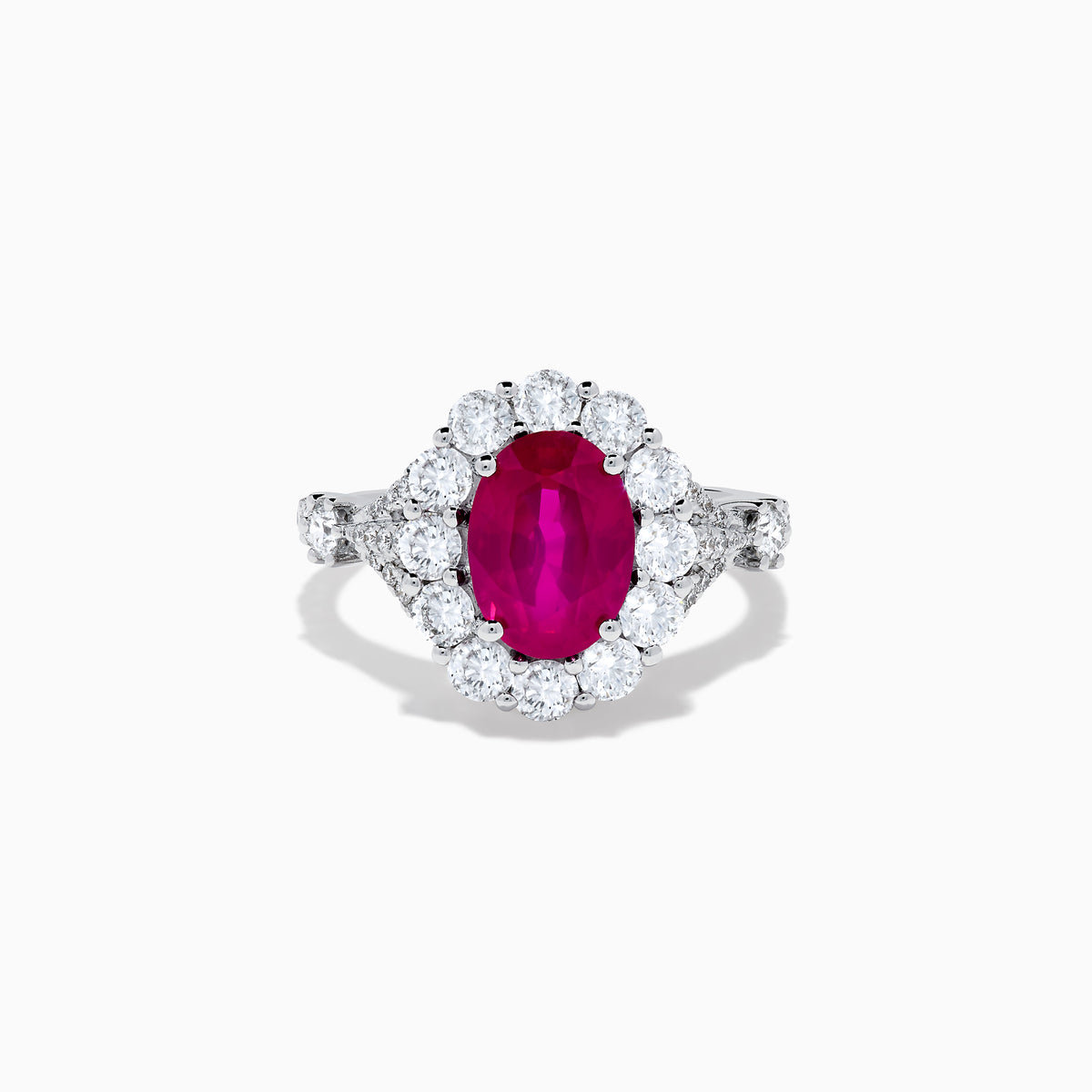 The 18K White Gold Ruby and Diamond Halo Ring features an oval red ruby at the center, encircled by a diamond halo, beautifully presented on a plain white background.