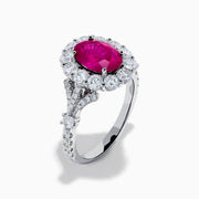 The 18K White Gold Ruby and Diamond Halo Ring features an oval red ruby at the center, encircled by a diamond halo, beautifully presented on a plain white background.