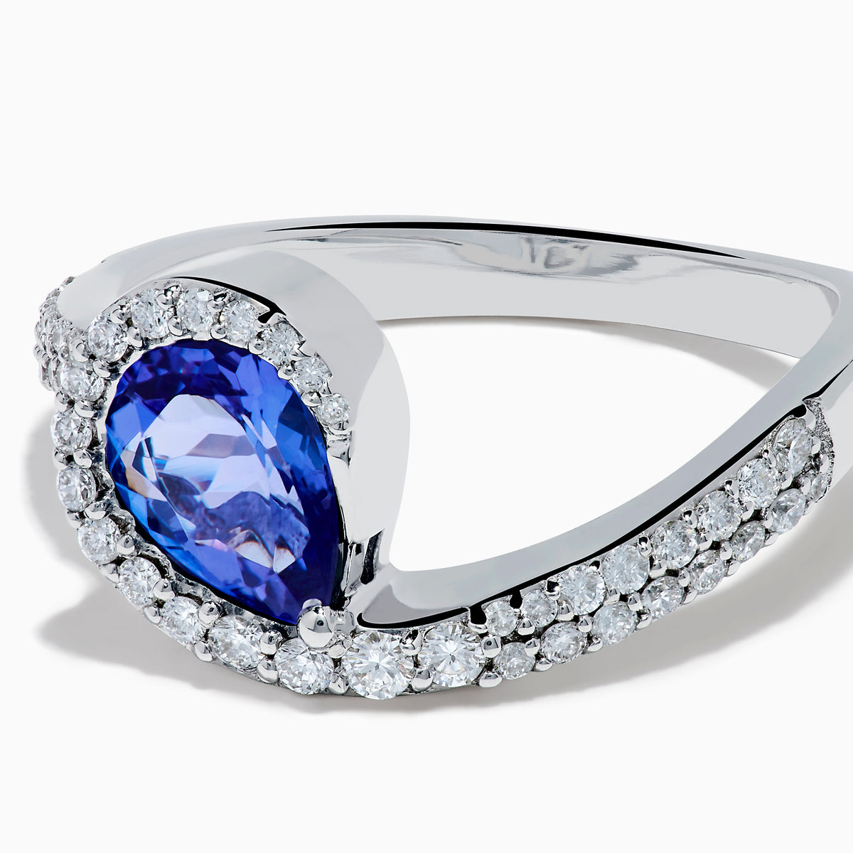 The Nahla 14K White Gold Tanzanite and Diamond Pear Swirl Ring showcases a pear-shaped blue tanzanite center, haloed by diamonds and accented with diamonds along a sweeping band.