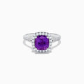 The 18K White Gold Purple Sapphire and Diamond Halo Ring showcases a cushion-cut purple sapphire center, encircled by a diamond halo and diamonds along the band.
