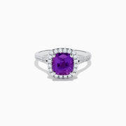 The 18K White Gold Purple Sapphire and Diamond Halo Ring showcases a cushion-cut purple sapphire center, encircled by a diamond halo and diamonds along the band.