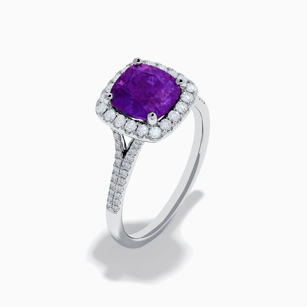 The 18K White Gold Purple Sapphire and Diamond Halo Ring showcases a cushion-cut purple sapphire center, encircled by a diamond halo and diamonds along the band.