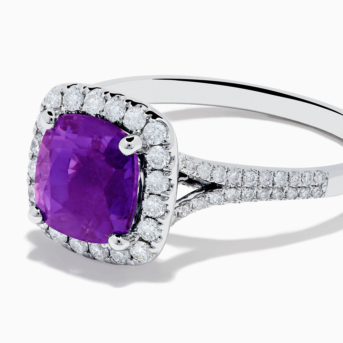 The 18K White Gold Purple Sapphire and Diamond Halo Ring showcases a cushion-cut purple sapphire center, encircled by a diamond halo and diamonds along the band.