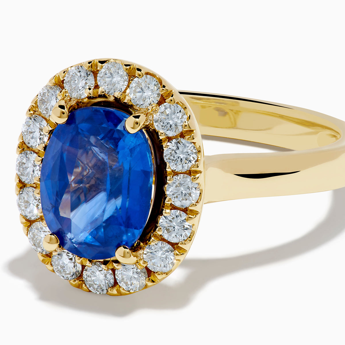 The Royale Bleu 18K Yellow Gold Blue Sapphire and Diamond Halo Ring showcases a striking oval blue sapphire centerpiece surrounded by a sparkling diamond halo.