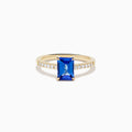 The Nahla 14K Yellow Gold Tanzanite and Diamond Ring showcases a rectangular blue tanzanite center stone, accented by small round white diamonds along the upper band on a plain white background—timeless elegance in every detail.