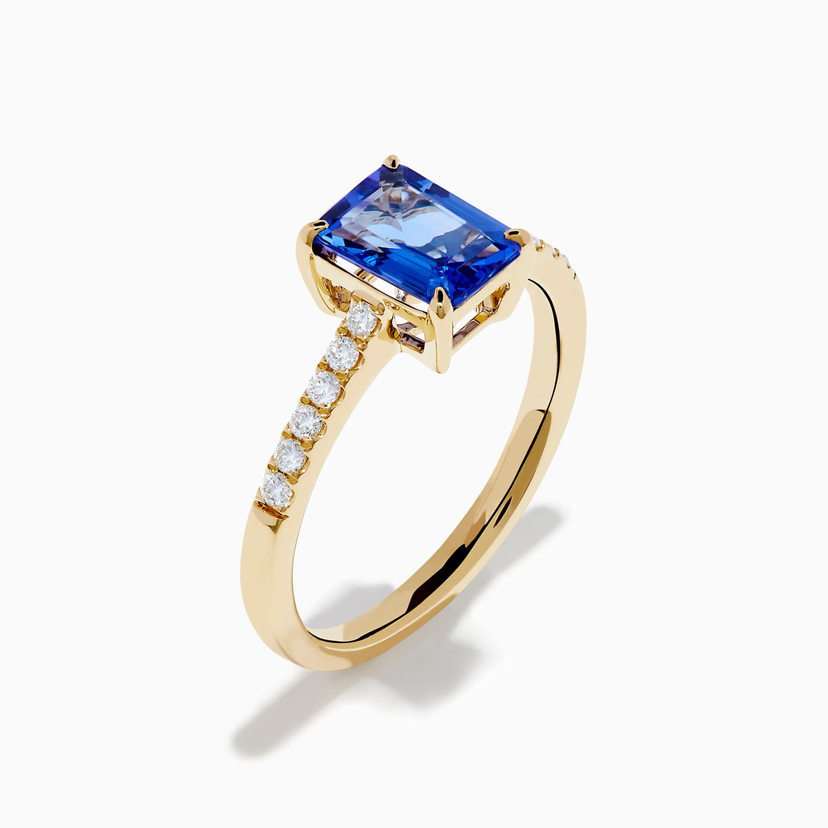 The Nahla 14K Yellow Gold Tanzanite and Diamond Ring showcases a rectangular blue tanzanite center stone, accented by small round white diamonds along the upper band on a plain white background—timeless elegance in every detail.