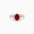 The Ruby Royale 14K Yellow Gold Ruby and Diamond 3 Stone Ring showcases a central oval ruby flanked by sparkling diamonds, set on a diamond-accented band and elegantly displayed against a white background.