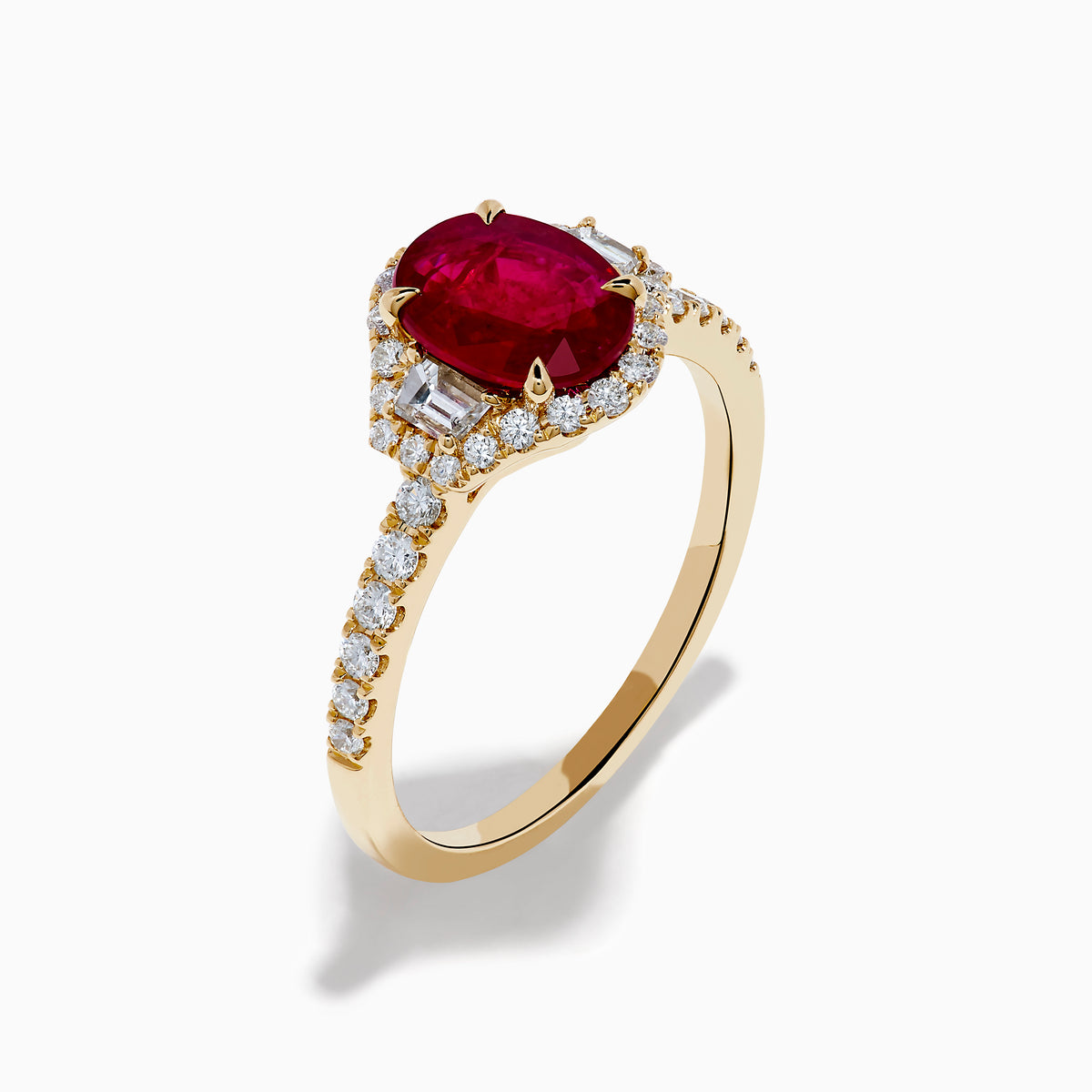 The Ruby Royale 14K Yellow Gold Ruby and Diamond 3 Stone Ring showcases a central oval ruby flanked by sparkling diamonds, set on a diamond-accented band and elegantly displayed against a white background.