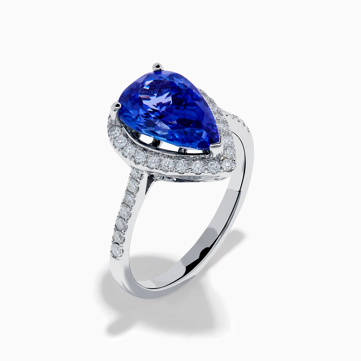 The Nahla 14K White Gold Tanzanite and Diamond Halo Ring features a pear-shaped tanzanite surrounded by diamonds on a slender, diamond-encrusted band, beautifully displayed on a white background.