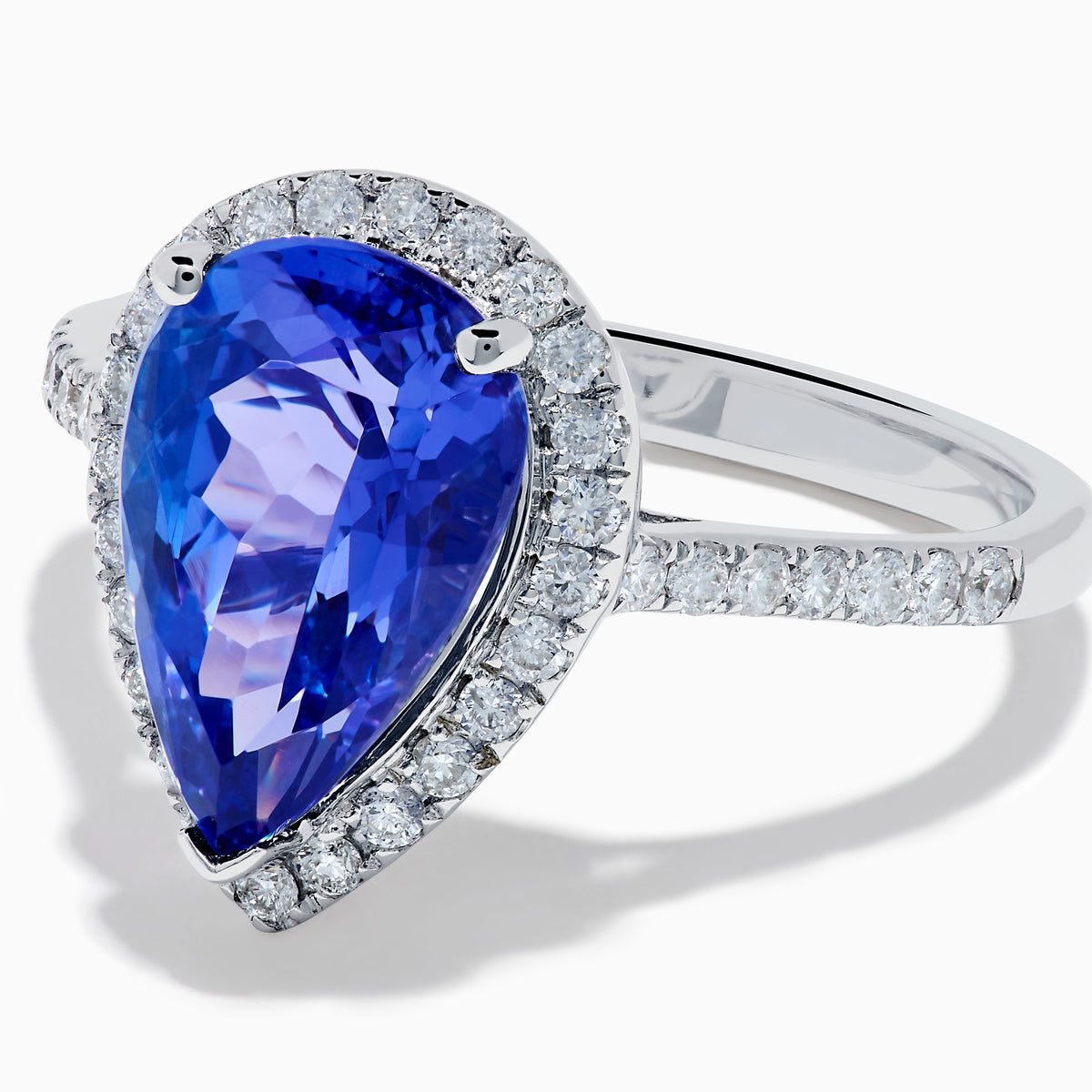 The Nahla 14K White Gold Tanzanite and Diamond Halo Ring features a pear-shaped tanzanite surrounded by diamonds on a slender, diamond-encrusted band, beautifully displayed on a white background.