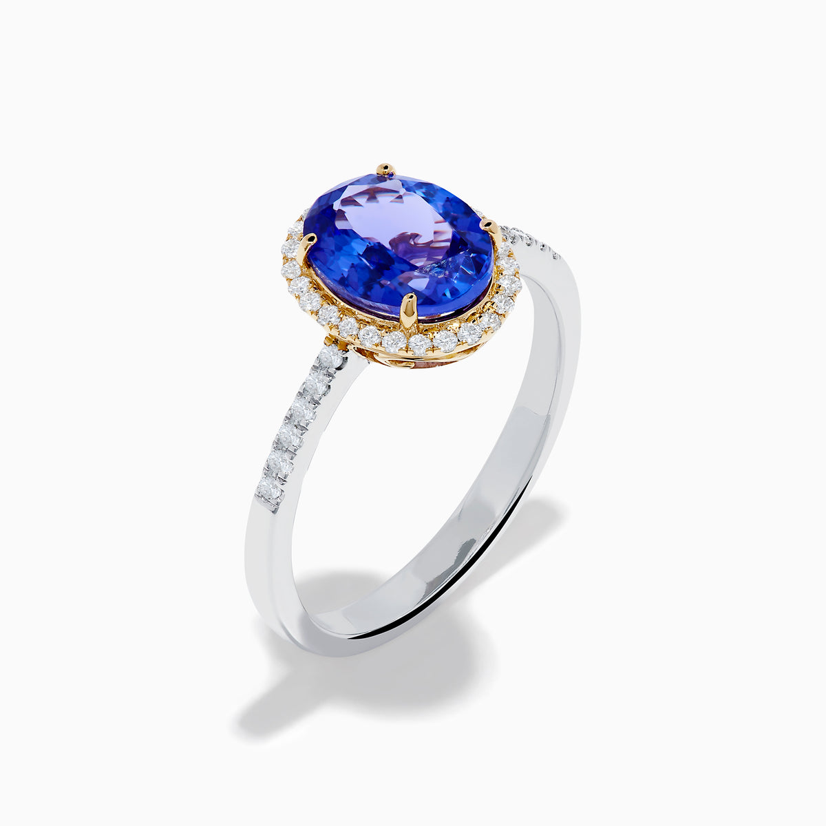 The Nahla 14K Two Tone Gold Tanzanite and Diamond Halo Ring features an oval blue tanzanite center, encircled by a diamond halo and diamond-accented band, all set in elegant two-tone 14K gold.