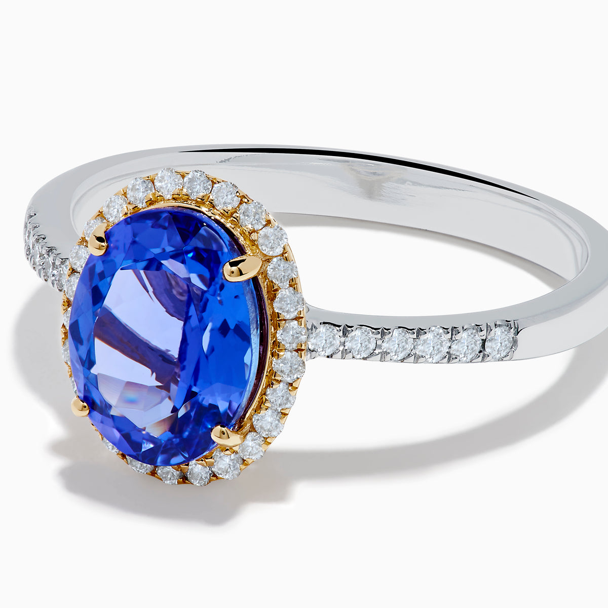 The Nahla 14K Two Tone Gold Tanzanite and Diamond Halo Ring features an oval blue tanzanite center, encircled by a diamond halo and diamond-accented band, all set in elegant two-tone 14K gold.