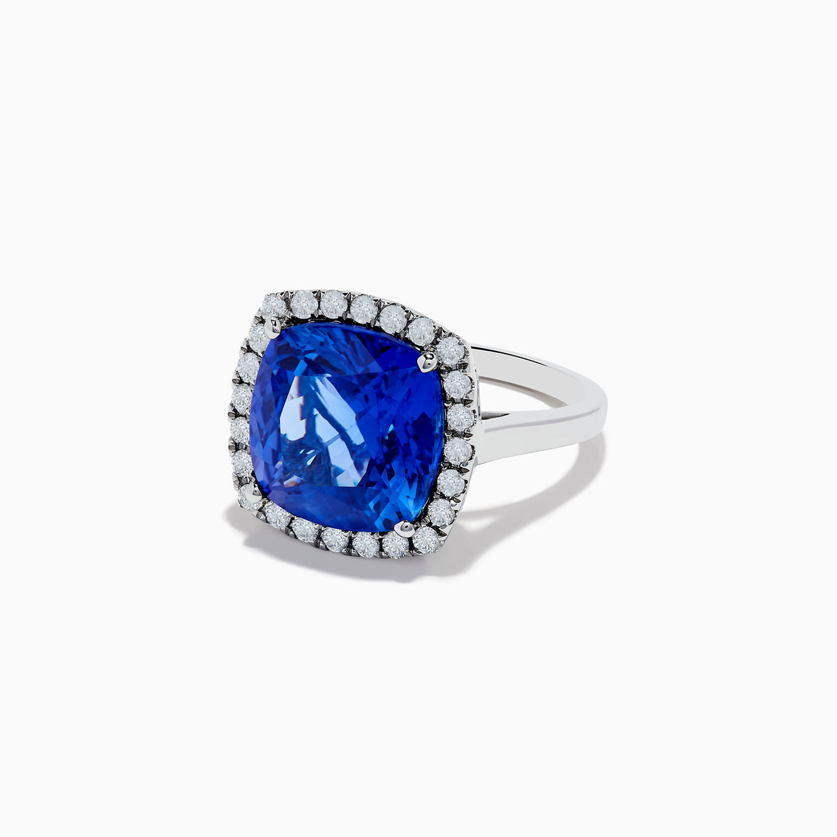 The Hematian 14K White Gold Tanzanite and Diamond Ring showcases a cushion-cut tanzanite center stone encircled by a halo of round diamonds, elegantly displayed on a white background.