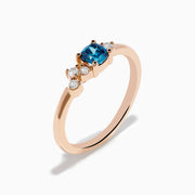 The 14K Rose Gold Blue and White Diamond Ring features a square-cut blue gemstone at the center with small round white diamonds on one side, displayed on a plain white background.
