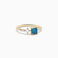 The 14K Yellow Gold Blue and White Diamond Ring features a square blue diamond, a smaller square white diamond, and three round white stones set asymmetrically on a plain band.