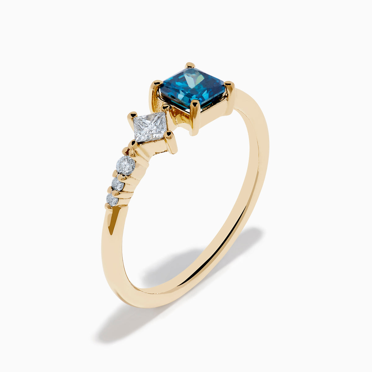 The 14K Yellow Gold Blue and White Diamond Ring features a square blue diamond, a smaller square white diamond, and three round white stones set asymmetrically on a plain band.