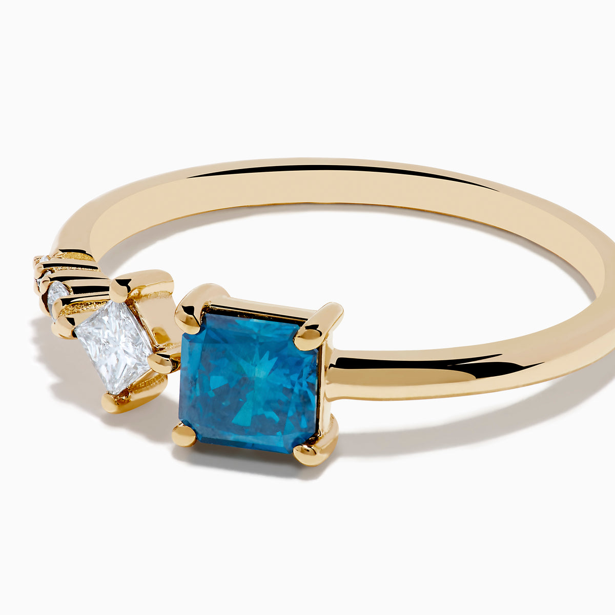 The 14K Yellow Gold Blue and White Diamond Ring features a square blue diamond, a smaller square white diamond, and three round white stones set asymmetrically on a plain band.