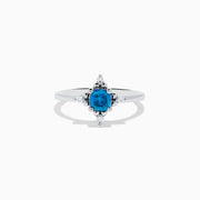 The 14K White Gold Blue and White Diamond Ring features a round blue diamond center with small white stones in a compass pattern, displayed on a white background.