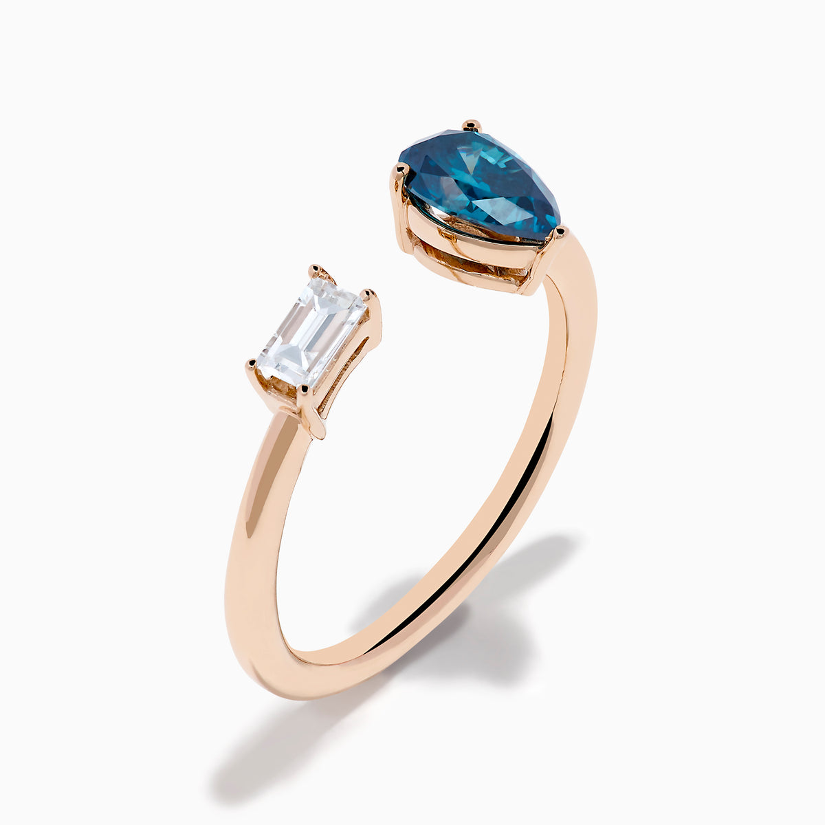 The 14K Rose Gold Blue and White Diamond Toi Et Moi Ring features an open design with a clear rectangular diamond and a blue teardrop diamond, elegantly displayed on a white background.